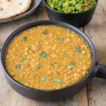 A black serving bowl with Indian dal, peas, rice and naan bread