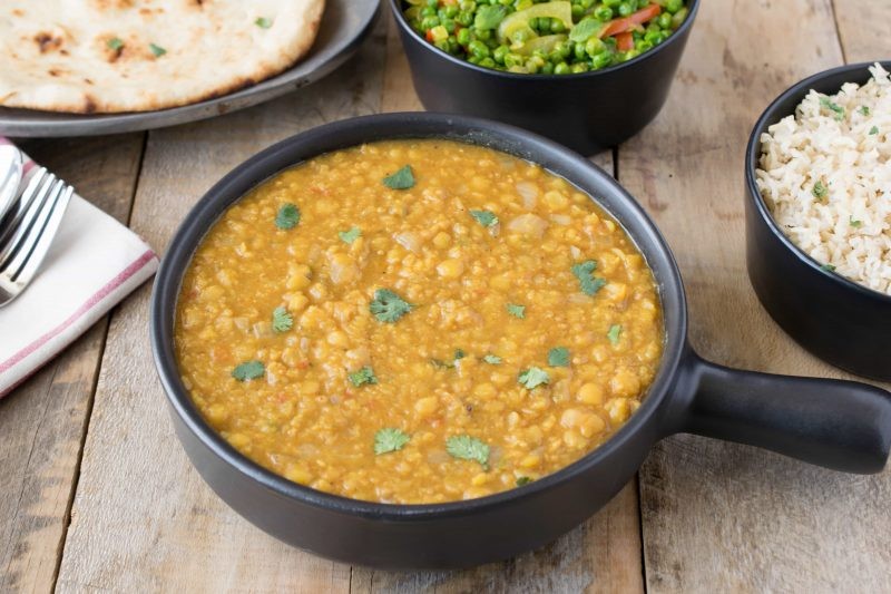 A black serving bowl with Indian dal, peas, rice and naan bread