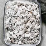 A clear glass dish filled with muddy buddies, showcasing their powdered sugar coating.