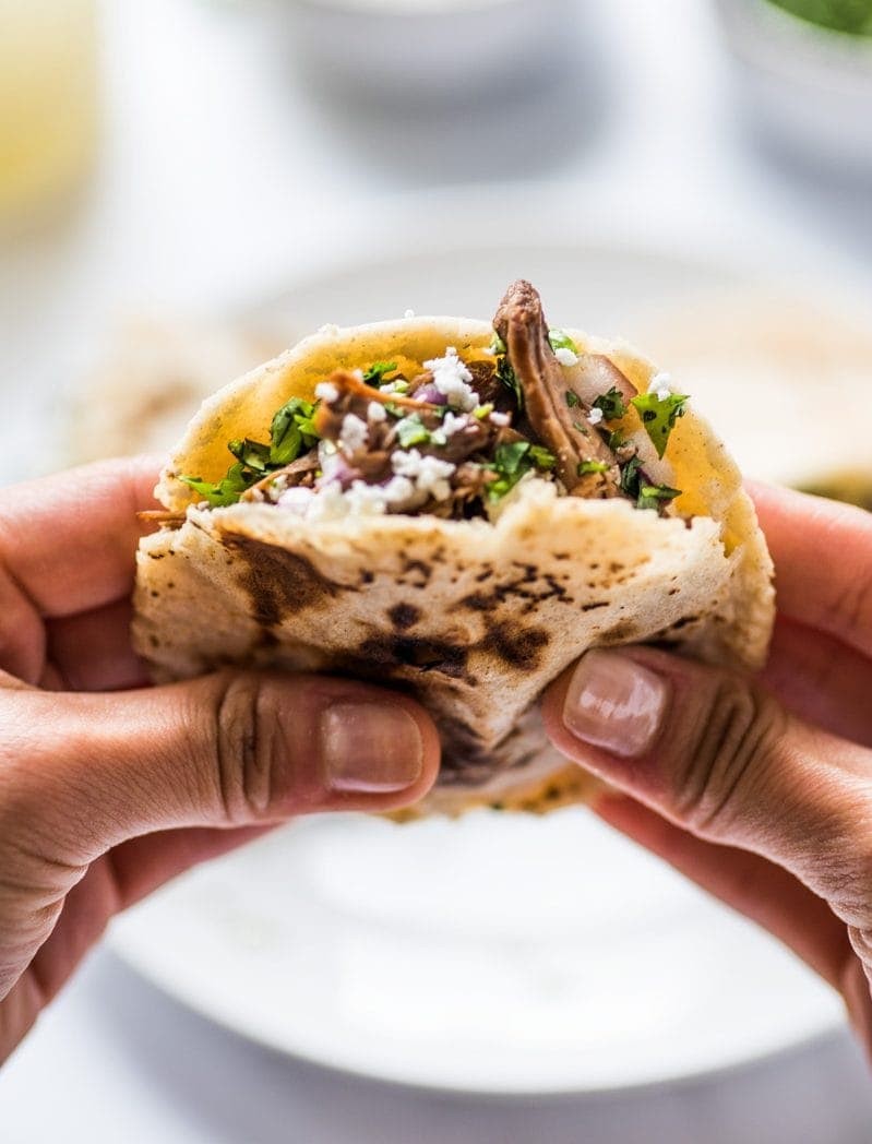 A close-up of a gordita filled with barbacoa beef, cheese, and cilantro, held in a hand.