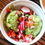 A close-up of Oso's guacamole topped with radishes, onions, and tomatoes, served with tortilla chips, highlighting fresh ingredients and vibrant colors.