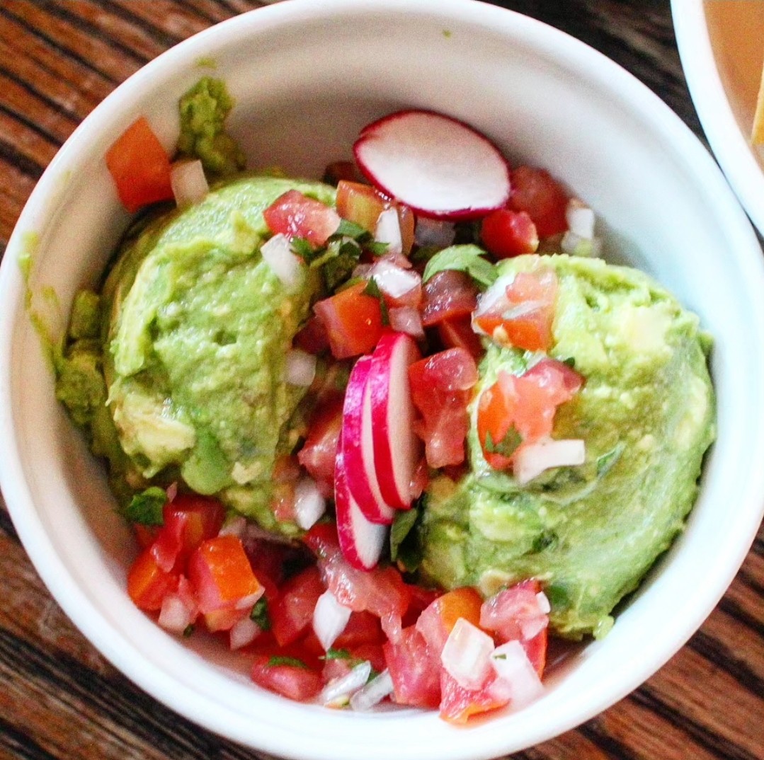 A close-up of Oso's guacamole topped with radishes, onions, and tomatoes, served with tortilla chips, highlighting fresh ingredients and vibrant colors.