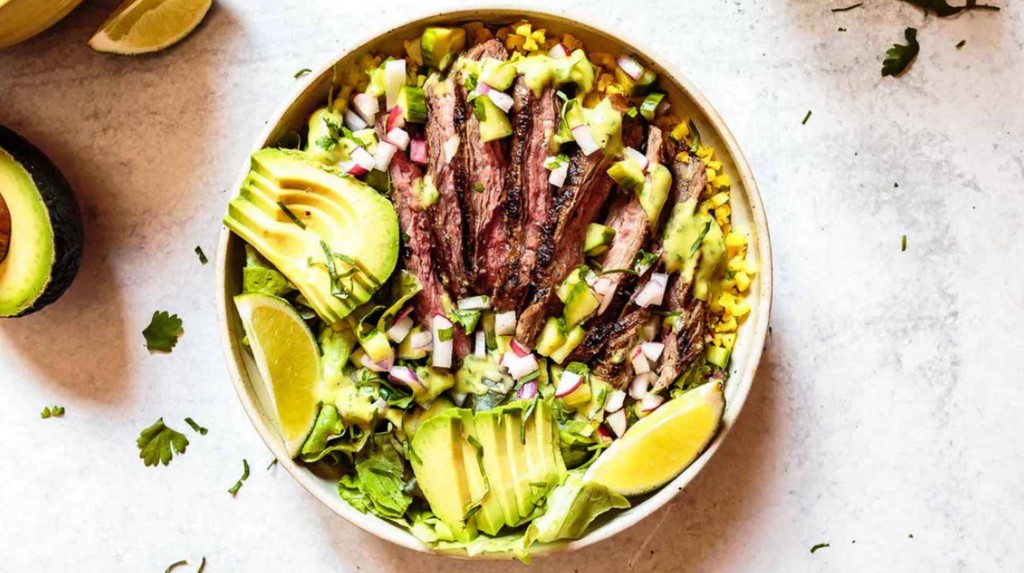 A close-up shot of a juicy grass-fed steak being cooked in a cast iron skillet, surrounded by herbs and garlic, representing high-quality meat for the Whole30 diet.