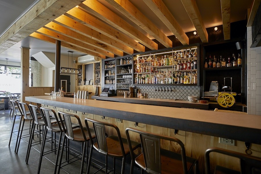 A dimly lit restaurant bar area with patrons seated at the bar and tables, showcasing a lively atmosphere.