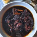 A flavorful bowl of Guyanese Pepperpot, a national dish, served with traditional plait bread.