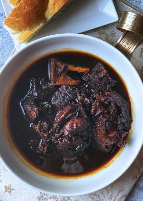 A flavorful bowl of Guyanese Pepperpot, a national dish, served with traditional plait bread.