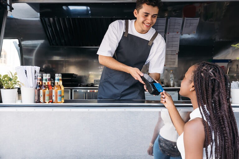 A food truck vendor accepting a credit card payment from a customer, illustrating POS system usage.