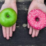 A fresh apple next to a glazed donut, visually representing the choice between unprocessed and ultra-processed food options.