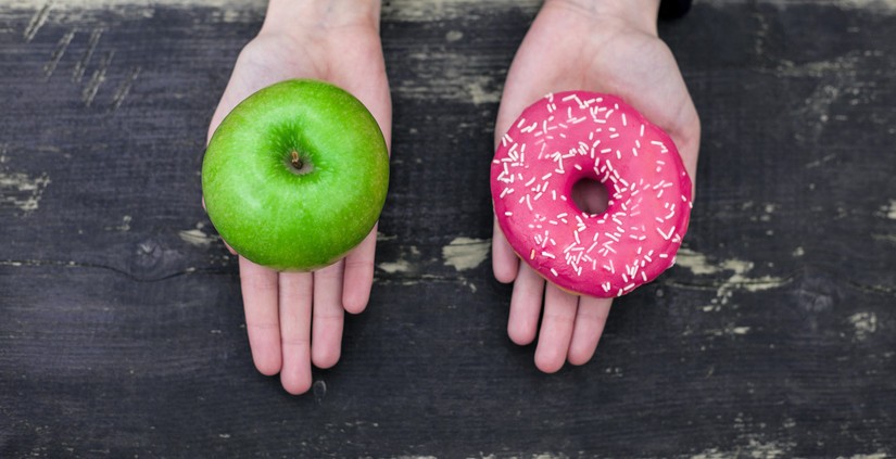 A fresh apple next to a glazed donut, visually representing the choice between unprocessed and ultra-processed food options.