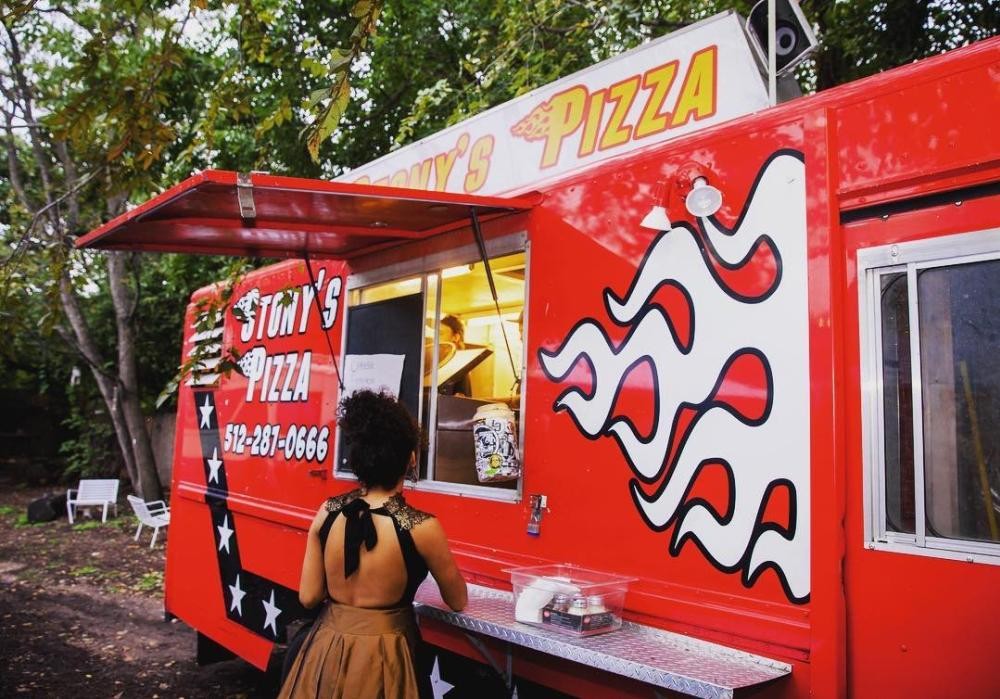 A friendly woman serves pizza slices from a food truck window, highlighting the personalized service of food trucks catering.