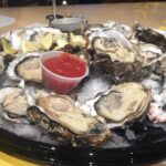 A half-order of enormous oysters served at Whole Foods happy hour, showcasing the generous portion and fresh seafood deal.