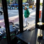 A pedestrian glances up at the "Thai Food Near Me" restaurant sign in New York City.