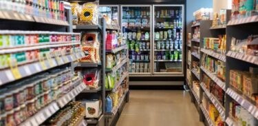 A person pushing a shopping cart in a grocery store aisle filled with produce, symbolizing grocery shopping for closeby food.