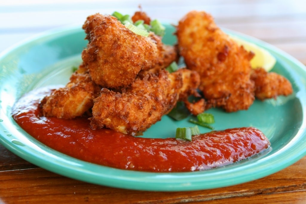 A plate of golden conch fritters, served with a dipping sauce, showcasing the crispy exterior and tender interior