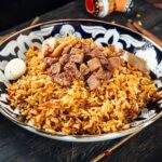 A plate of Uyghur Polo, showcasing rice, carrots, and lamb, a signature dish of Xinjiang, China