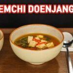 A steaming bowl of Korean Soybean Paste Soup (Doenjang Guk) with visible spinach and tofu, showcasing a comforting and savory breakfast option.