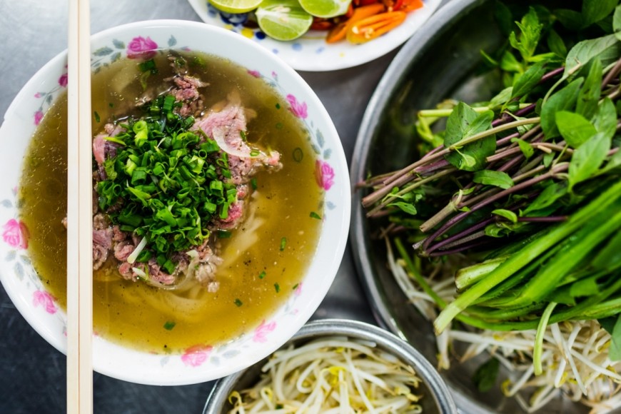 A steaming bowl of Pho, showcasing the rich broth and fresh herbs