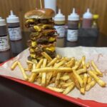 A towering bacon burger challenge at This Guy’s Smoke and Grill in Searcy, Arkansas, featuring layers of beef, bacon, cheese, and a side of fries.