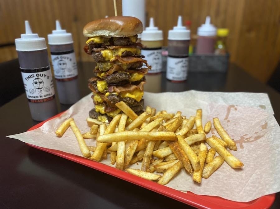 A towering bacon burger challenge at This Guy’s Smoke and Grill in Searcy, Arkansas, featuring layers of beef, bacon, cheese, and a side of fries.