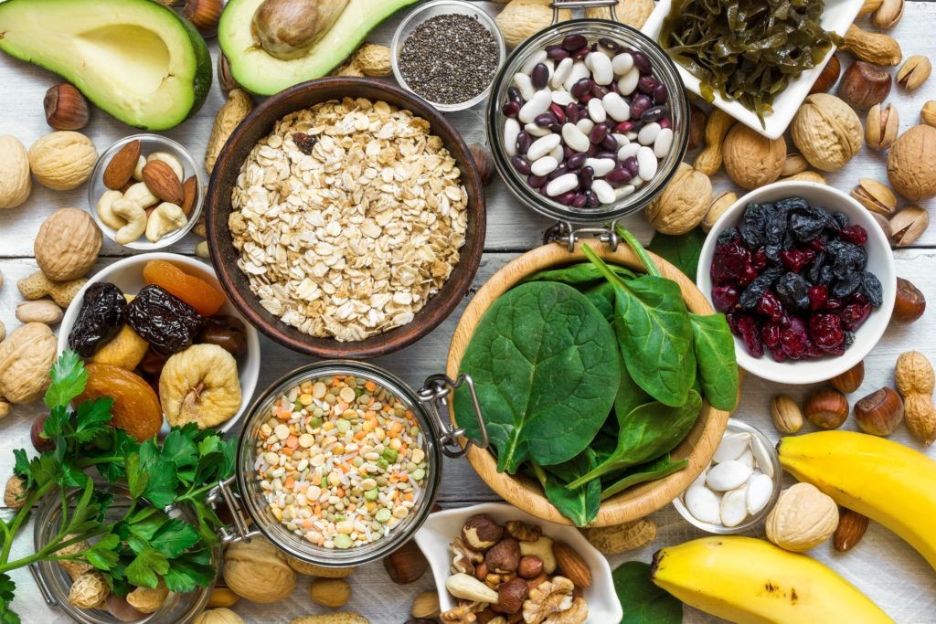 A vibrant display of magnesium-rich foods including bananas, avocados, nuts like almonds and walnuts, seeds such as chia and pumpkin, leafy greens like spinach, lentils, peas, oats, rice, dried apricots, and kelp, highlighting diverse dietary sources of magnesium.