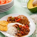 A vibrant Dominican lunch featuring rice, beans, chicken, salad, and avocado.