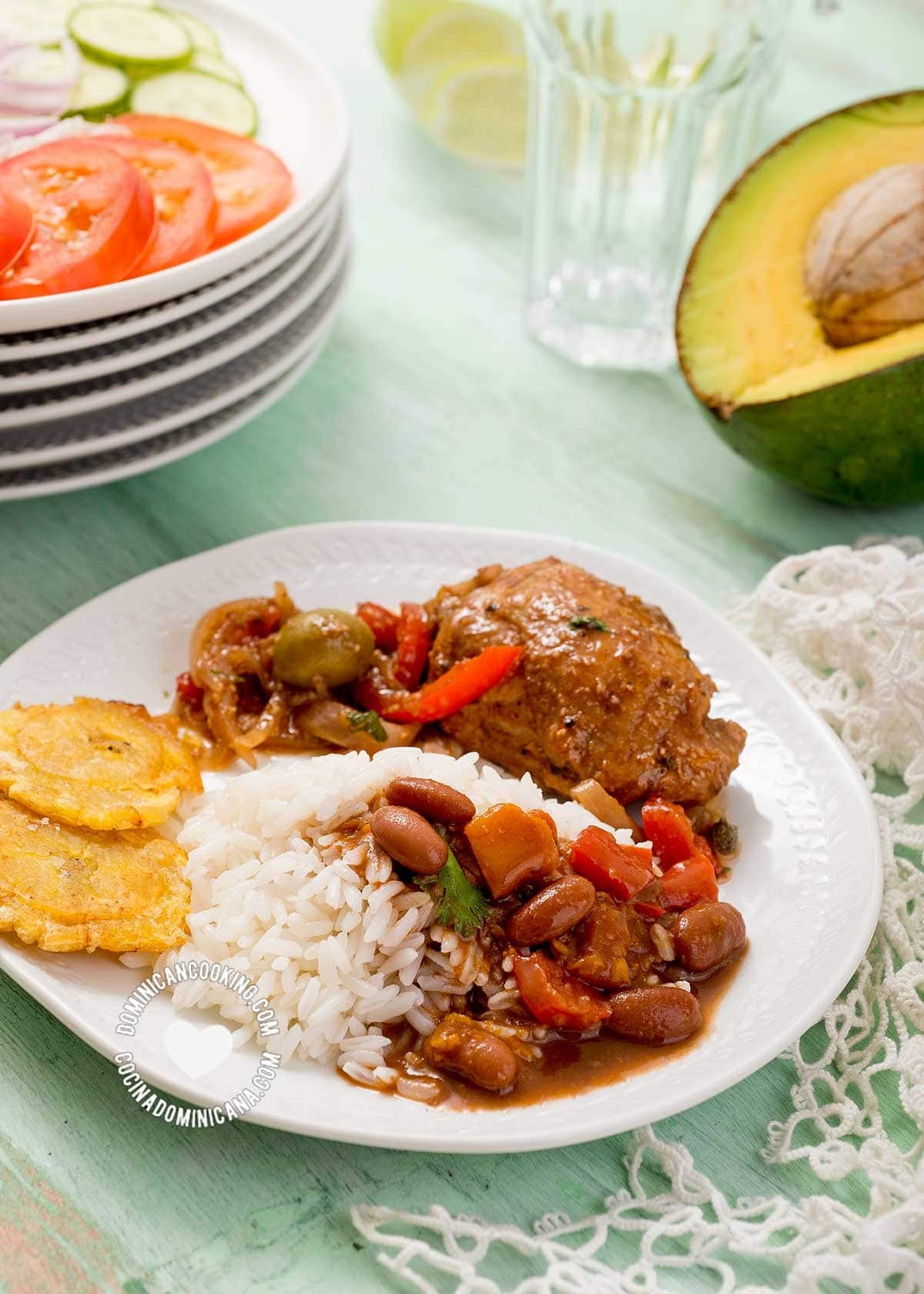 A vibrant Dominican lunch featuring rice, beans, chicken, salad, and avocado.