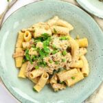 A vibrant green plate of cream cheese pasta, perfectly cooked and garnished, with forks elegantly placed beside it.