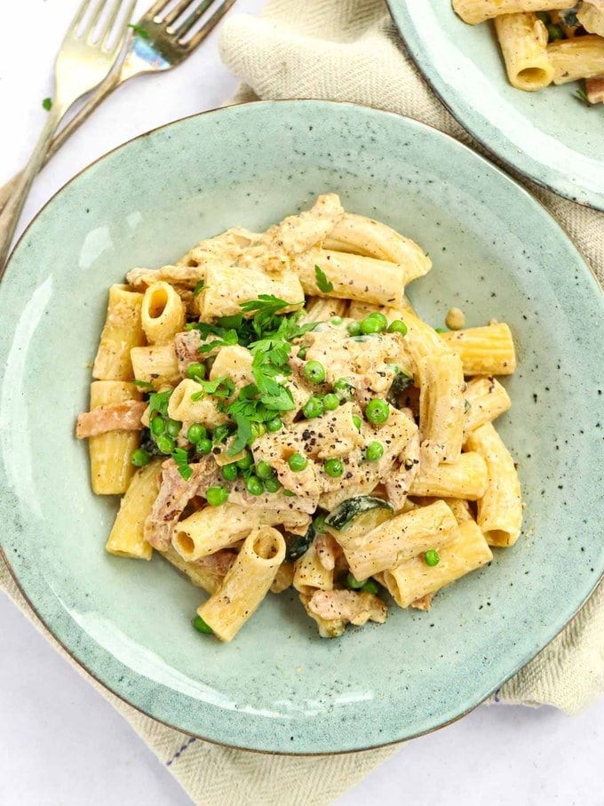 A vibrant green plate of cream cheese pasta, perfectly cooked and garnished, with forks elegantly placed beside it.