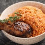 A vibrant plate of Jollof Rice, a staple Nigerian African food dish, showcasing its reddish hue and steam, surrounded by serving utensils.