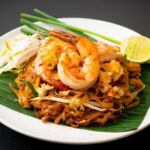 A vibrant plate of Pad Thai, showcasing noodles, shrimp, tofu, peanuts, and lime.