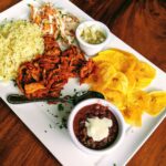 A vibrant plate of typical Nicaraguan food, showcasing gallo pinto, plantains, and cheese on a rustic brown table.