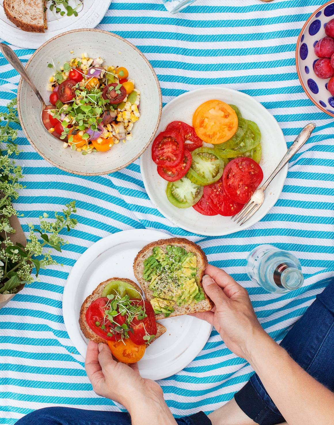 A vibrant spread of picnic food including sandwiches, salads, and fruits, laid out on a checkered blanket in a sunny outdoor setting.