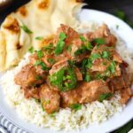 A white plate with rice, chicken tikka masala, and naan.