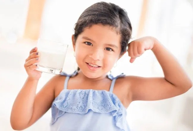 A young girl happily drinking milk, symbolizing strength and healthy development.