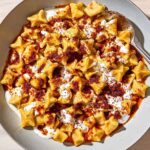 An overhead photo of manti topped with garlic yogurt and spiced oil in a bowl with a spoon.