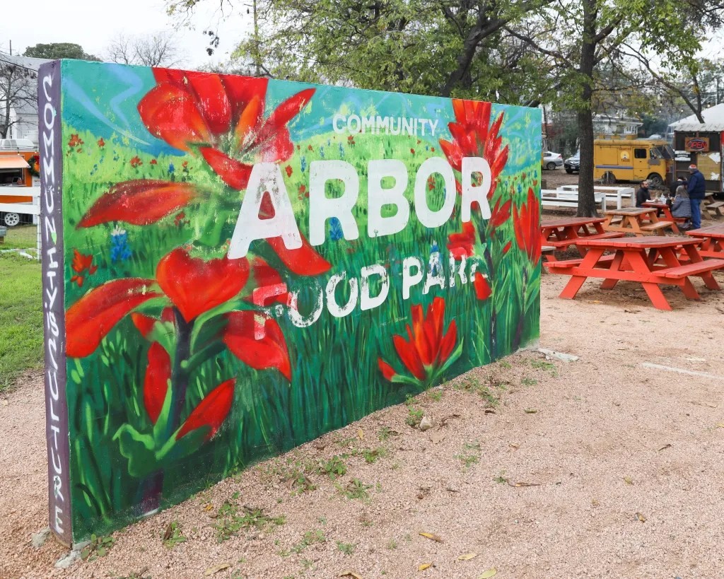 An overview of Arbor Food Park in Austin, Texas, showcasing a variety of food trucks and outdoor picnic table seating areas.