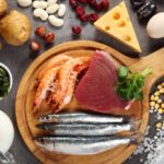 Assortment of iodine-rich foods including various types of fish like cod and tuna, shellfish such as oysters and shrimp, iodized salt, milk, different kinds of seaweed like nori and kelp, nuts and seeds, potatoes and beans, eggs, and dairy products like cheese and yogurt, displayed on a wooden surface.