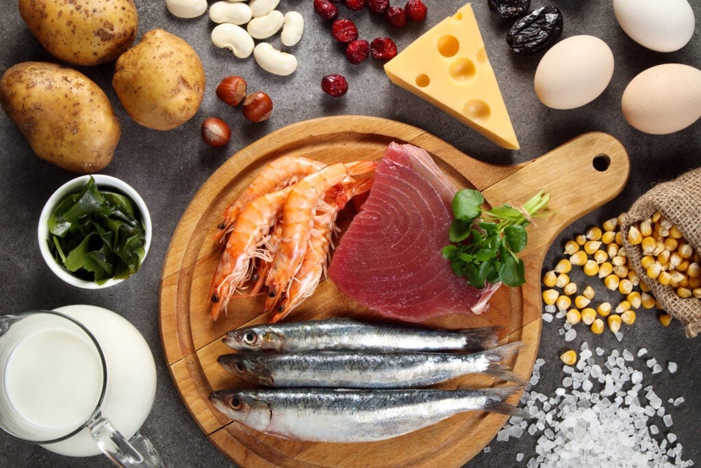 Assortment of iodine-rich foods including various types of fish like cod and tuna, shellfish such as oysters and shrimp, iodized salt, milk, different kinds of seaweed like nori and kelp, nuts and seeds, potatoes and beans, eggs, and dairy products like cheese and yogurt, displayed on a wooden surface.