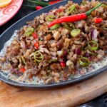 Authentic Filipino Pork Sisig Recipe served sizzling hot on a metal plate.