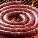 Boerewors sausage coiled on a barbecue, sizzling and releasing flavorful smoke.