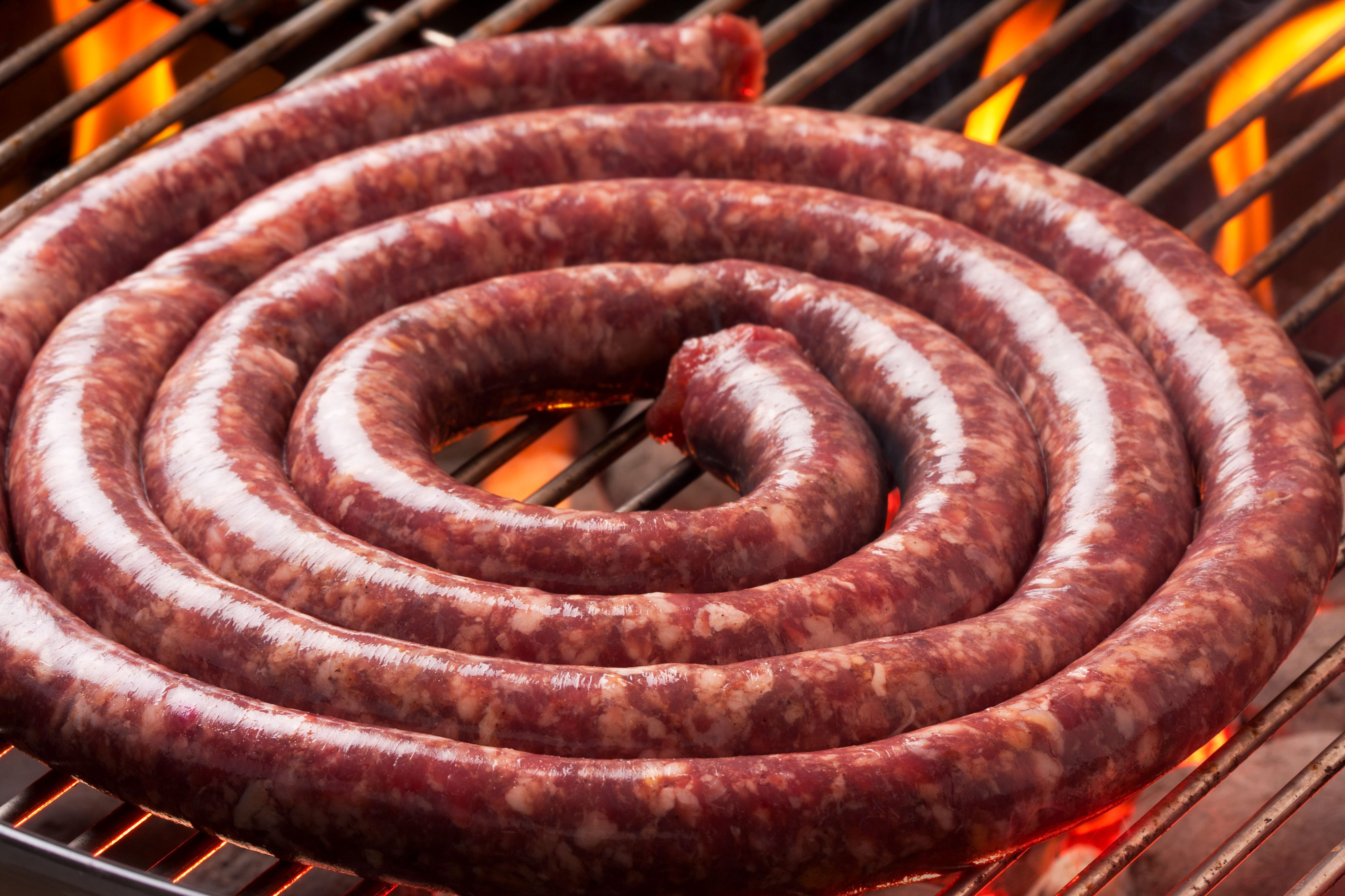 Boerewors sausage coiled on a barbecue, sizzling and releasing flavorful smoke.