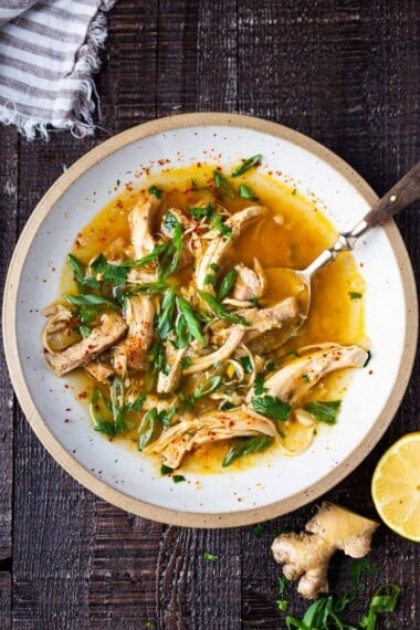 Bowl of Feel Better Chicken Soup with Lemon and Ginger, garnished with fresh herbs, in a cozy kitchen setting.