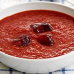 Bowl of vibrant red Gazpacho soup, garnished with fresh vegetables.