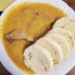 Bread dumplings are plated with a vegetable cream sauce and slow cooked beef sirloin in a traditional Czech dish