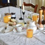 breakfast table set with china, orange juice, eggs, candles on white table cloth