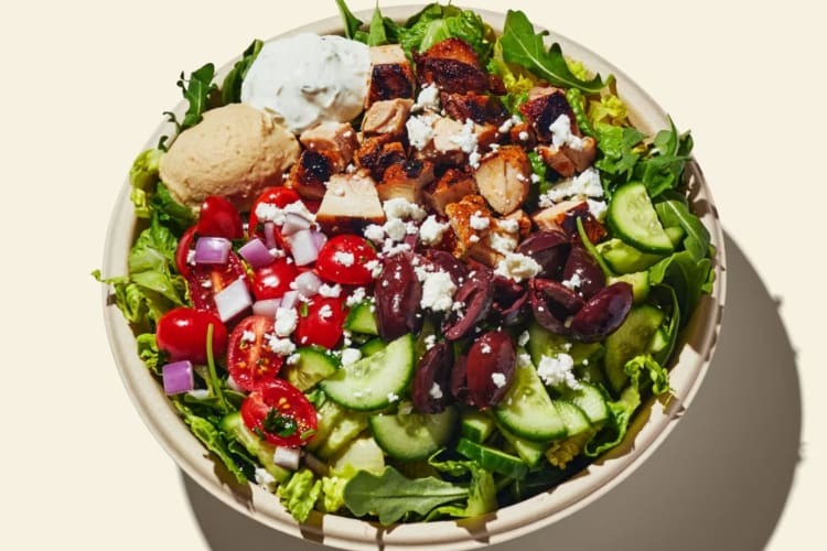 Cava Greek Salad ingredients including romaine, arugula, grilled chicken, tzatziki, feta, cucumber, tomato, Kalamata olives, Greek vinaigrette.