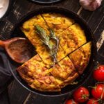 Close-up of a freshly made Tortilla Espanola, a traditional Spanish potato omelet, served in a rustic cast iron pan, showcasing its golden-brown crust and inviting texture, highlighting popular Hispanic food.