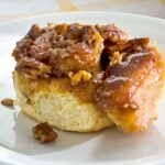 Close up of a kanelbulle (cinnamon bun) on a plate, showcasing its swirl and pecans.