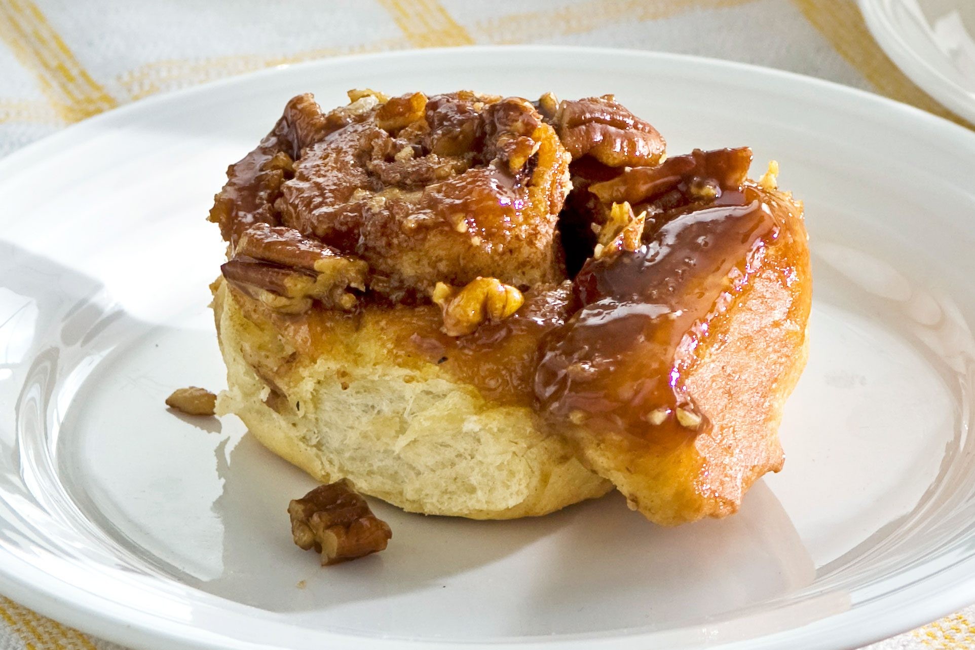 Close up of a kanelbulle (cinnamon bun) on a plate, showcasing its swirl and pecans.