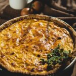 Close-up of a slice of Quiche Lorraine with visible layers of crust, filling, and bacon, showcasing its texture and ingredients.